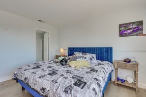 A bedroom with a bed, a nightstand, a lamp, a poster, and a door. - Long-term Getaway w/ Pool Access in Mission Viejo! (Mission Viejo)