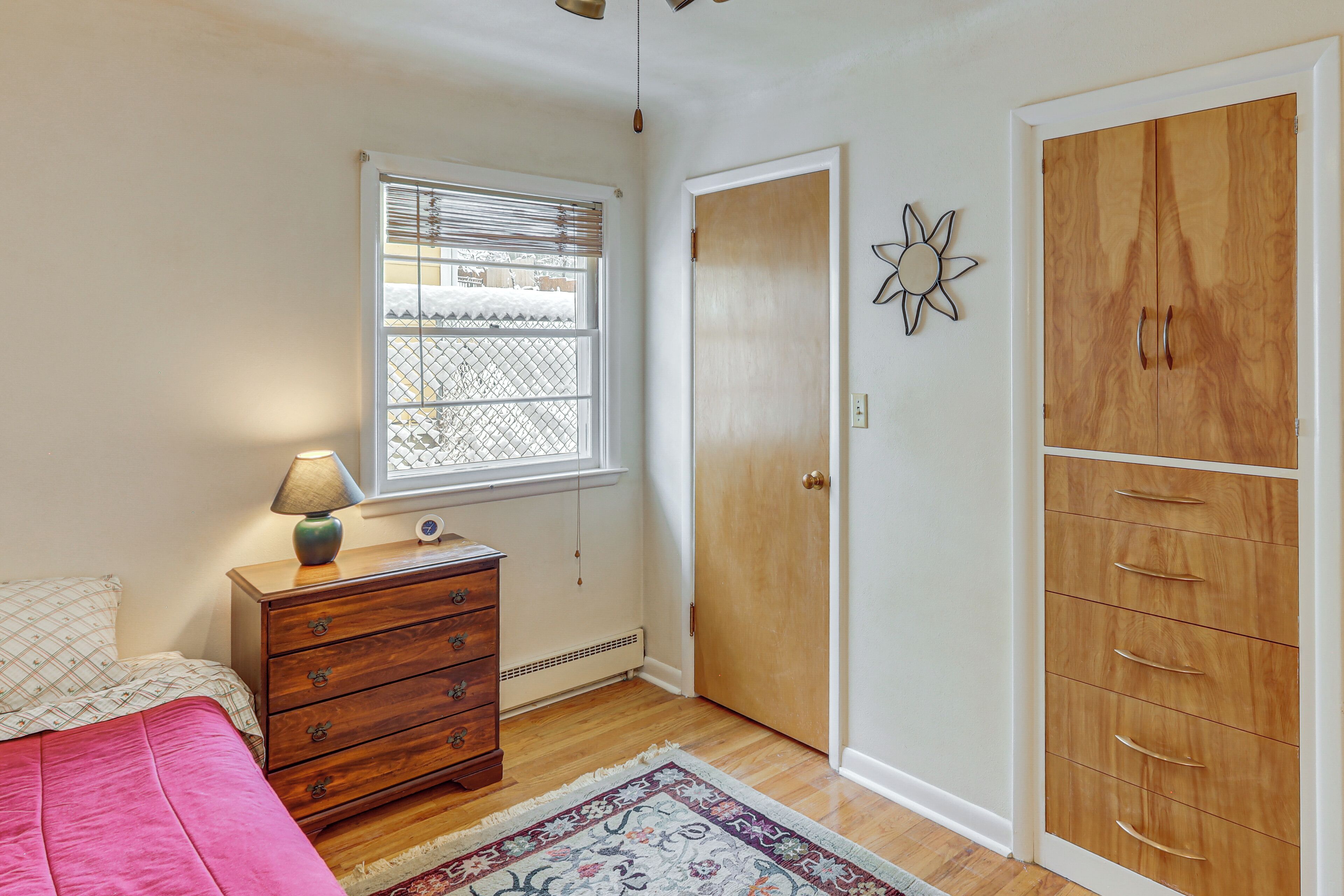 Une chambre à coucher comprenant un lit, une commode, une fenêtre avec des stores, une armoire et un élément décoratif mural.