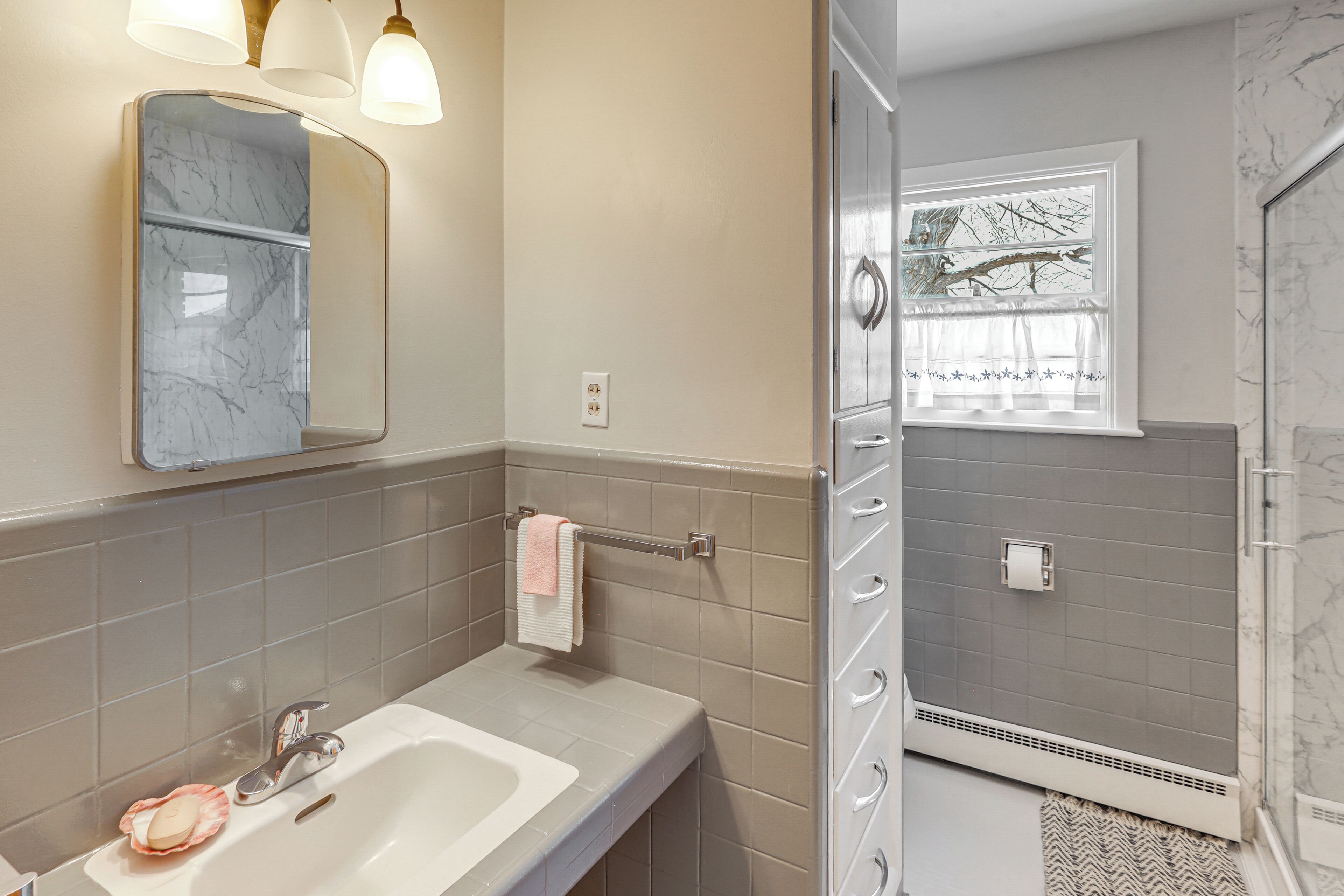A bathroom with a marble sink, a towel rack, a mirror, and a shower with a window.