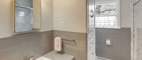A bathroom with a marble sink, a towel rack, a mirror, and a shower with a window.