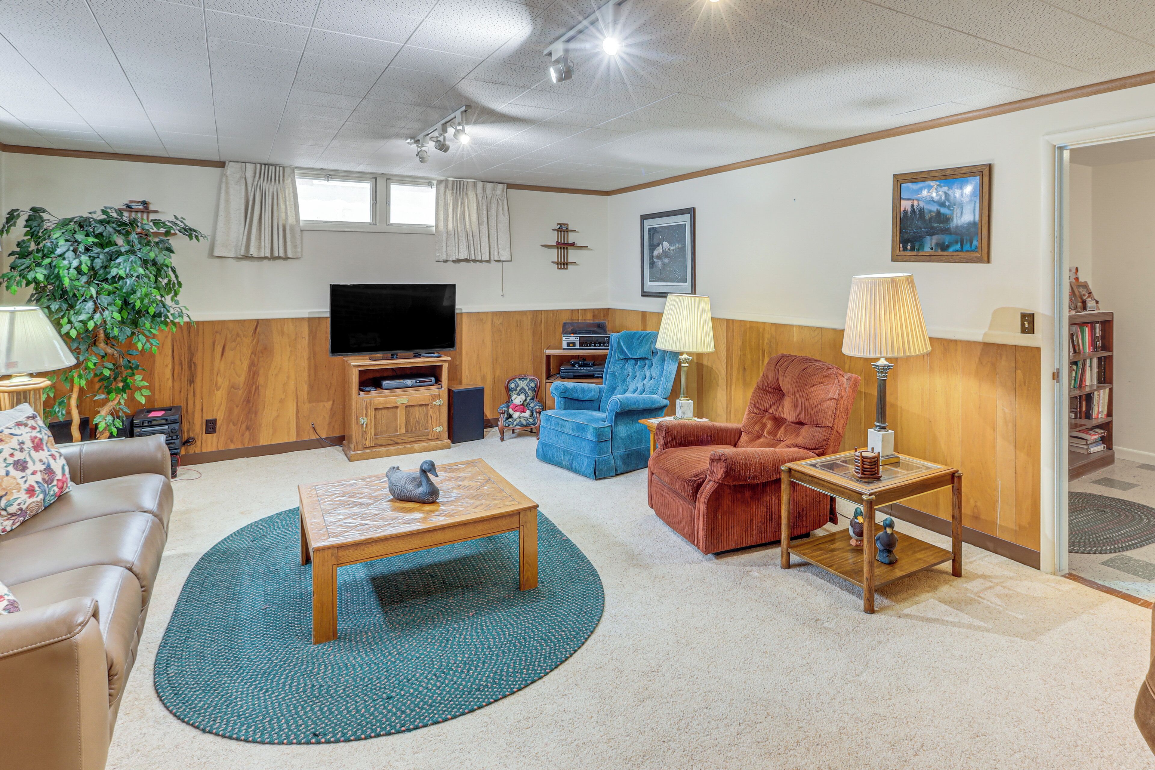 A living room with a television, a sofa, a coffee table, a blue armchair, a red armchair, and a lamp.
