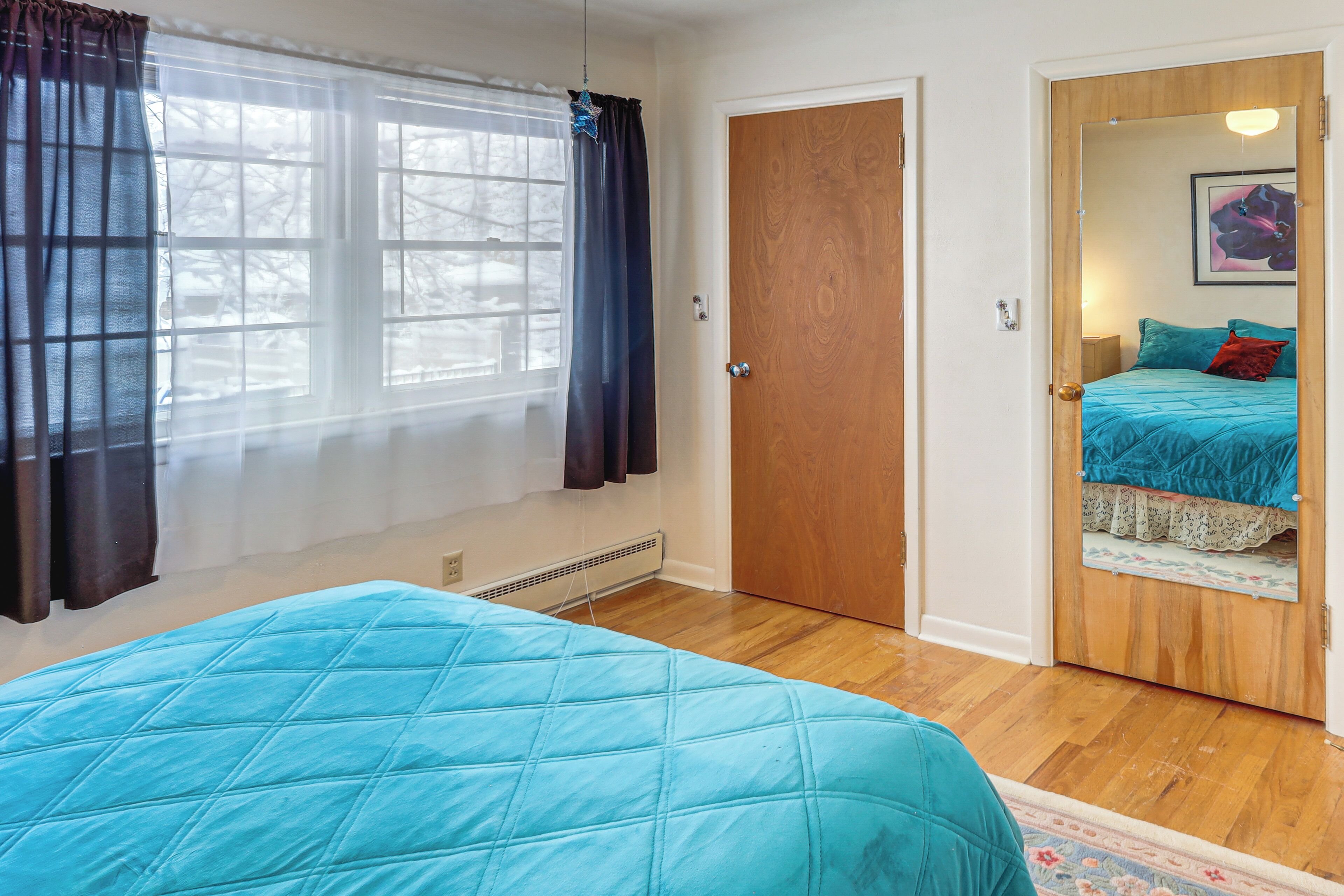 A bedroom with a bed, a door, and a window with curtains.