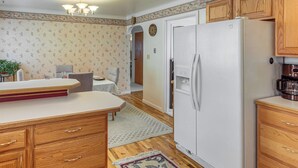 A kitchen with wooden cabinets, a white refrigerator, a dining table with chairs, and a clock on the wall.