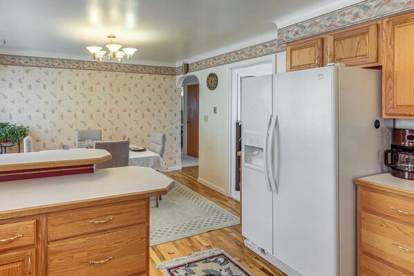 A kitchen with wooden cabinets, a white refrigerator, a dining table with chairs, and a clock on the wall.
