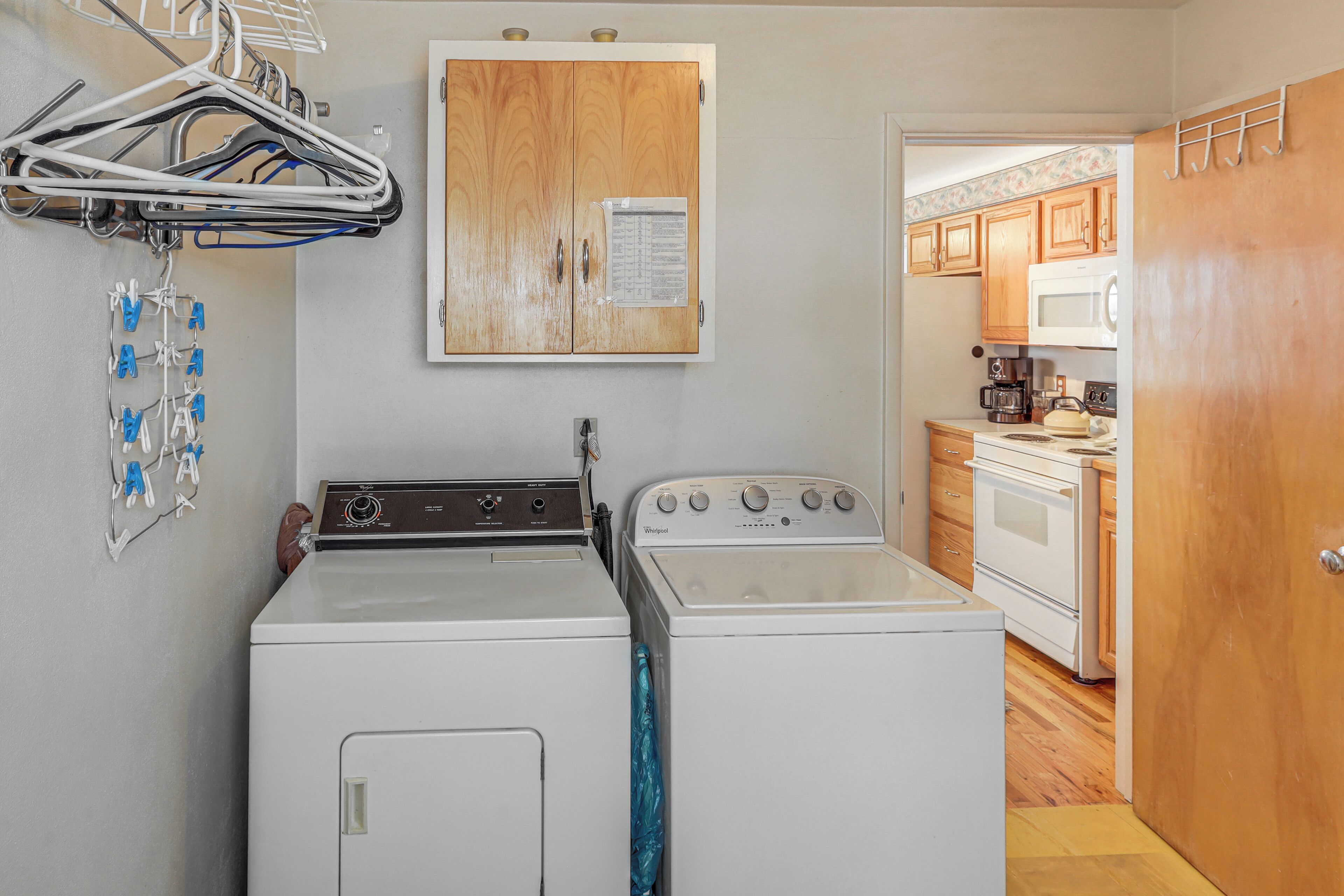 A laundry area with a washer and dryer, a wooden cabinet with a paper, and a kitchen with appliances.