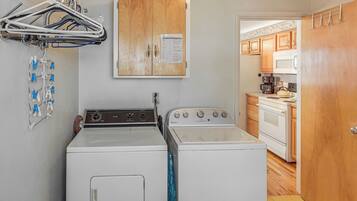 A laundry area with a washer and dryer, a wooden cabinet with a paper, and a kitchen with appliances.
