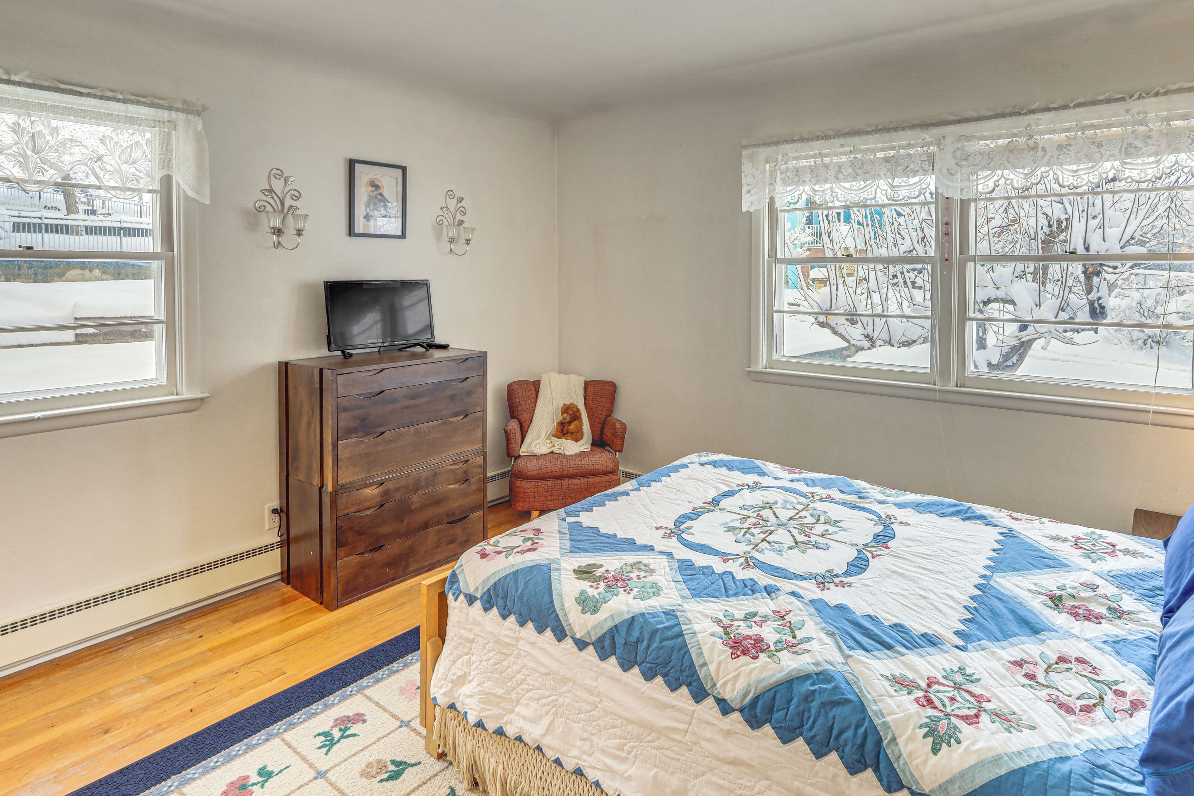 A bedroom with a bed, dresser, chair, and two windows.