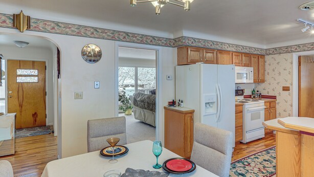 A dining area with a table set for four, a kitchen with wooden cabinets, a refrigerator, and a microwave.