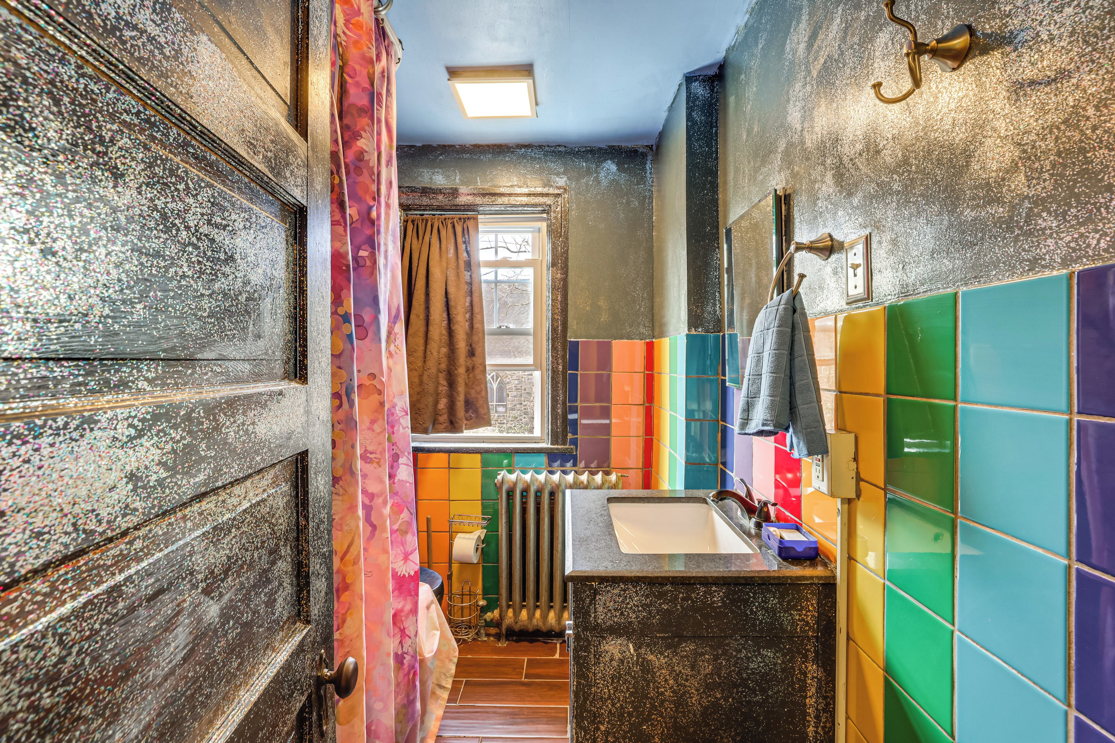 Un baño con puerta de madera, ventana, radiador y baldosas de colores.