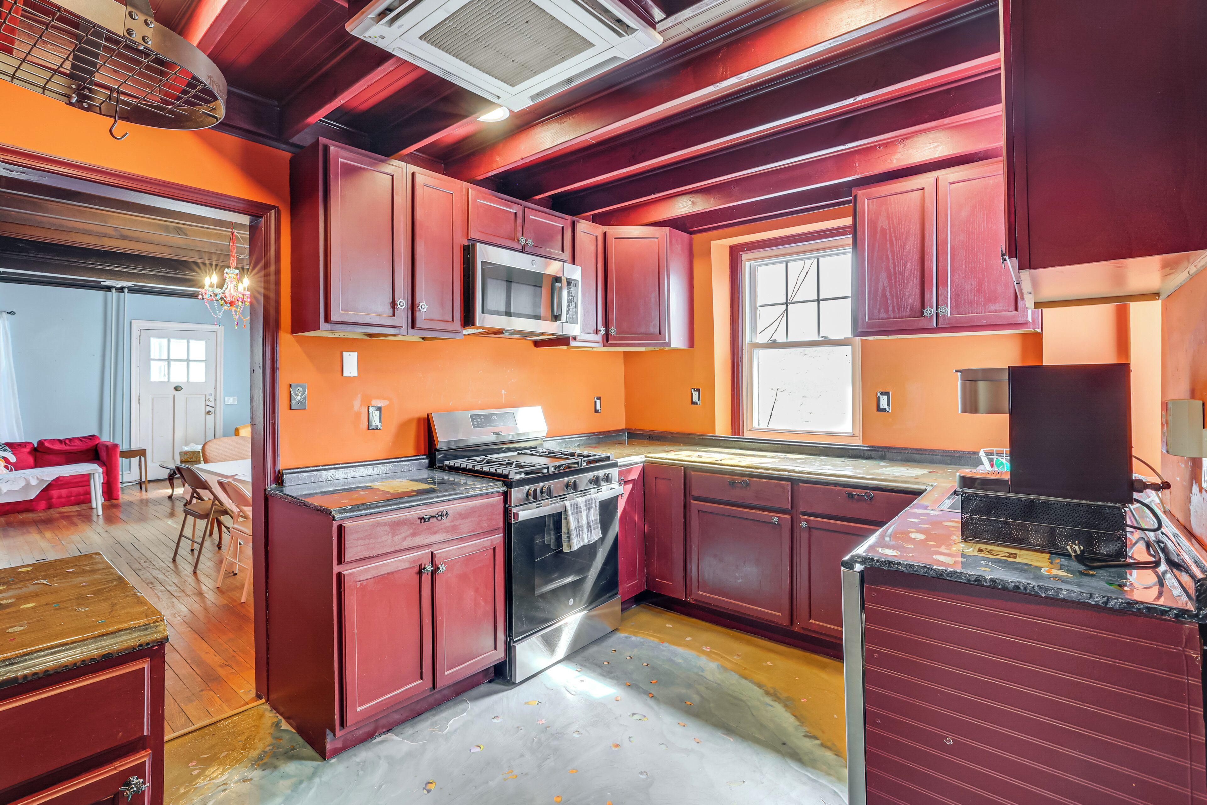 Una cocina con gabinetes rojos, estufa de acero inoxidable y microondas.