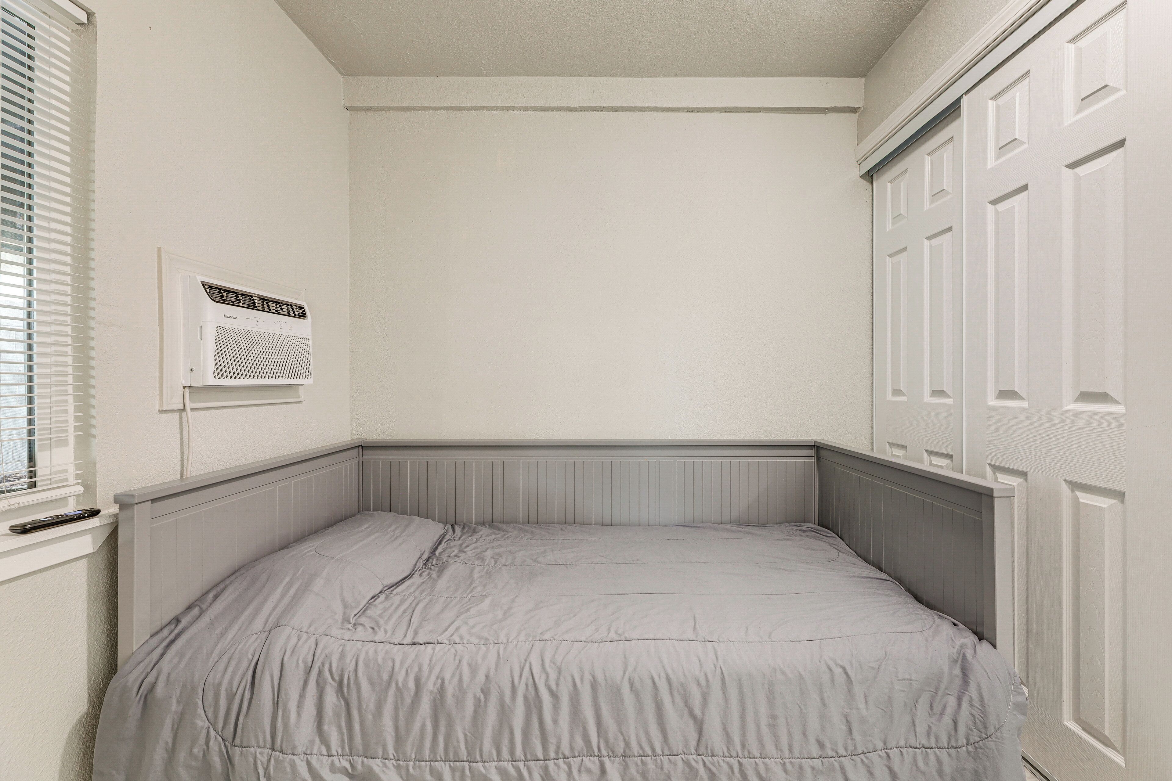 Une chambre avec un lit simple, une fenêtre avec des stores, un radiateur fixé au mur et une porte ornée d’un panneau décoratif.