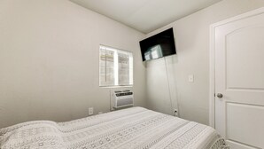 A bedroom with a bed, a TV mounted on the wall, a window with blinds, and an air conditioning unit. - Cozy & Convenient Condo in Compton, Pets Welcome! (Compton)