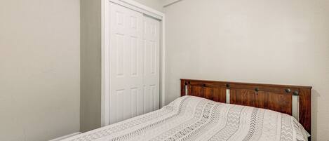 A bedroom with a wooden headboard, a patterned bedspread, and a white door.