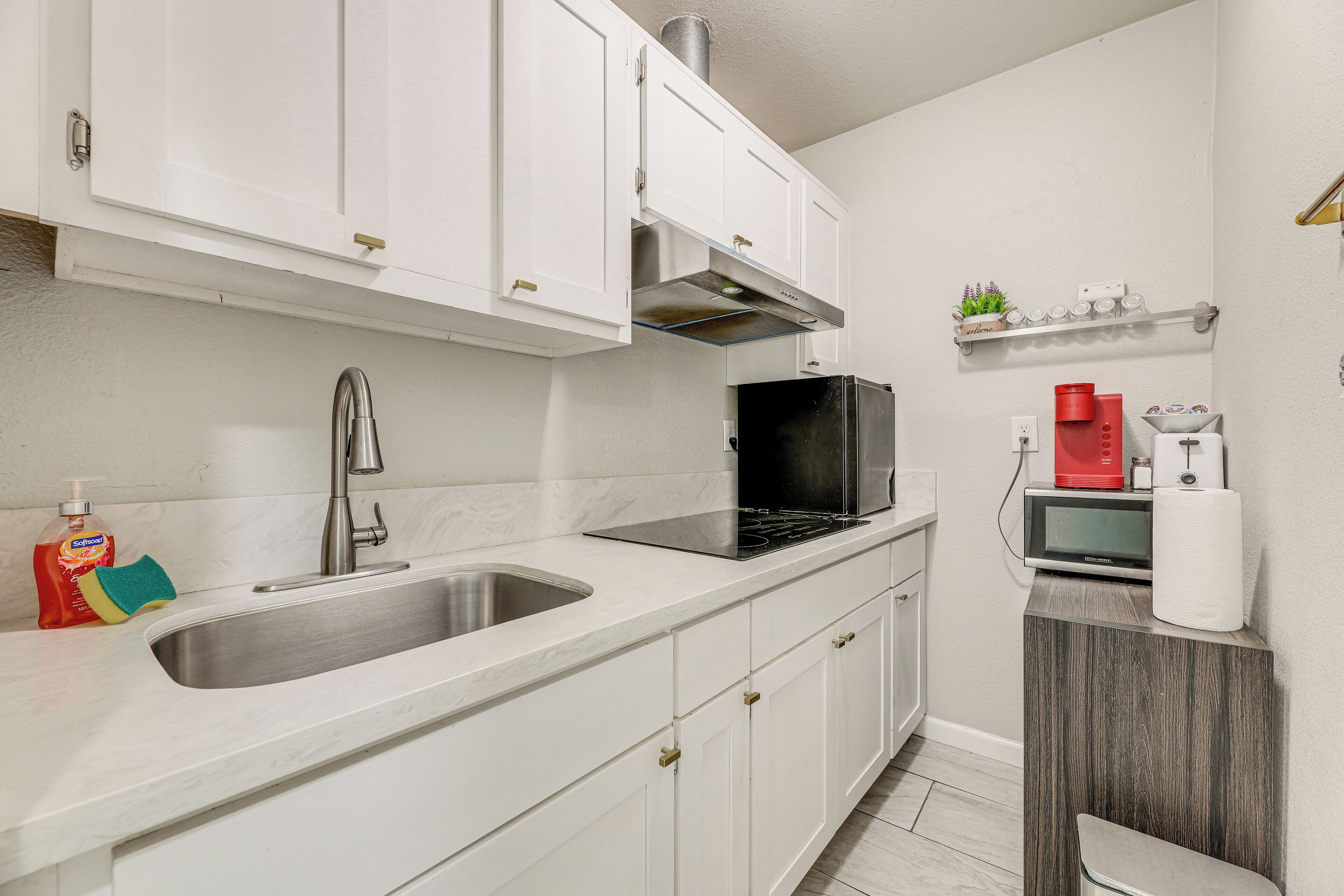 A modern kitchen with white cabinets, stainless steel sink, black microwave, and a coffee maker.
