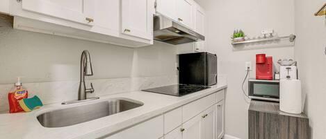 A modern kitchen with white cabinets, stainless steel sink, black microwave, and a coffee maker.