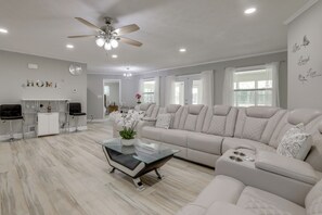 A modern living room with a sectional sofa, a glass coffee table, a ceiling fan, and a kitchen area in the background. - Sunroom & Spacious Yard! Woodsy Haven in Lilburn (Lilburn)