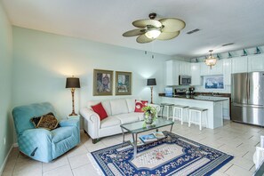 A living room with a sofa, armchair, coffee table, and a kitchen area with a refrigerator, microwave, and bar stools. - Stroll to Beach! 3BR Gulfport Escape, Pool Access (Gulfport)