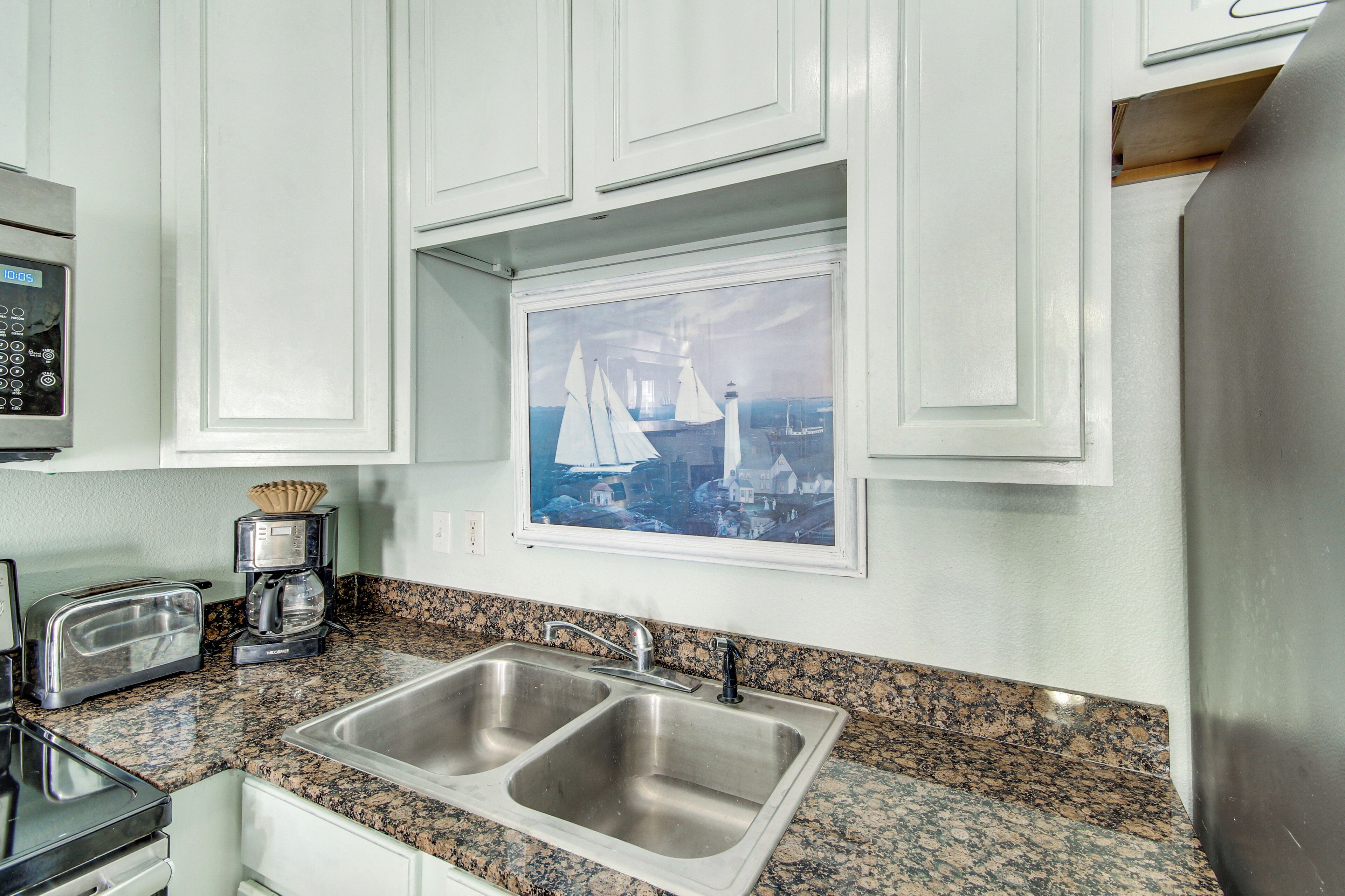 A kitchen with two stainless steel sinks, a toaster, a coffee maker, and a framed picture of sailboats on the wall.