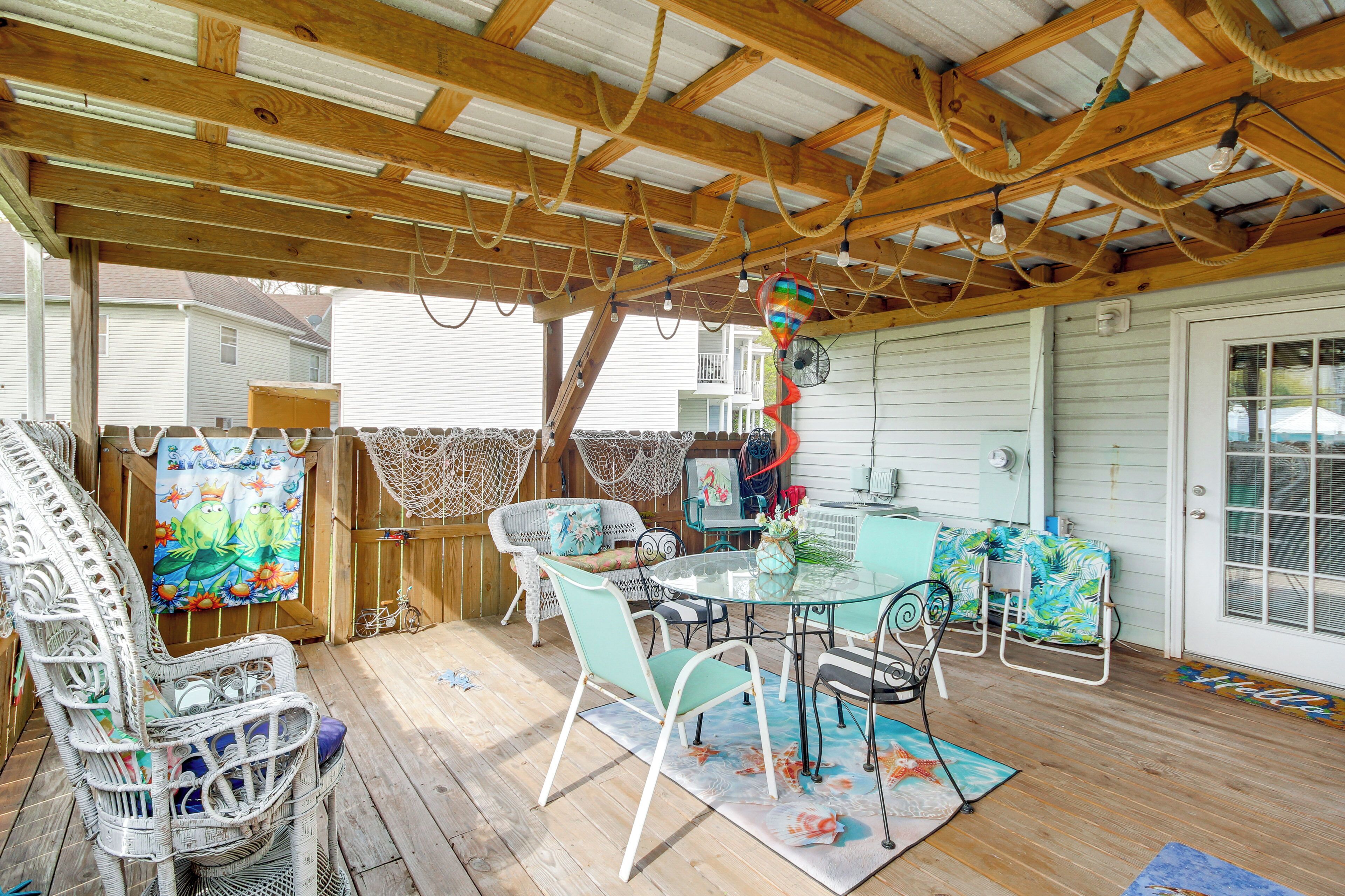 A covered outdoor patio with wicker furniture, a glass table, and a view of a house.