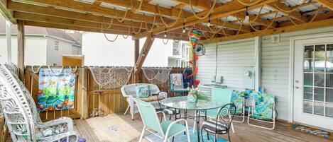 A covered outdoor patio with wicker furniture, a glass table, and a view of a house.
