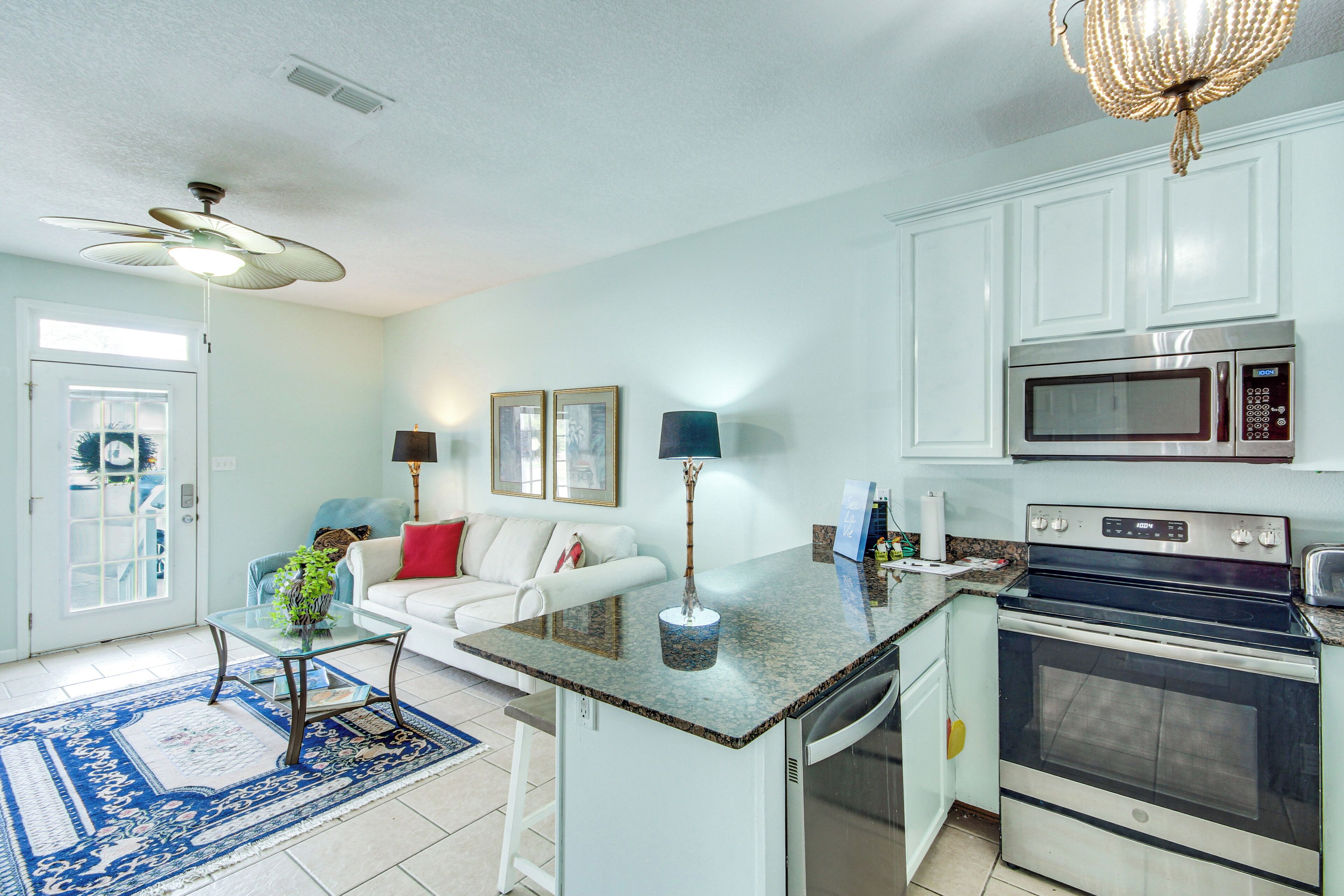 A kitchen with a microwave, oven, and a dining area with a white sofa and a glass coffee table.