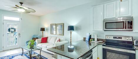 A kitchen with a microwave, oven, and a dining area with a white sofa and a glass coffee table.