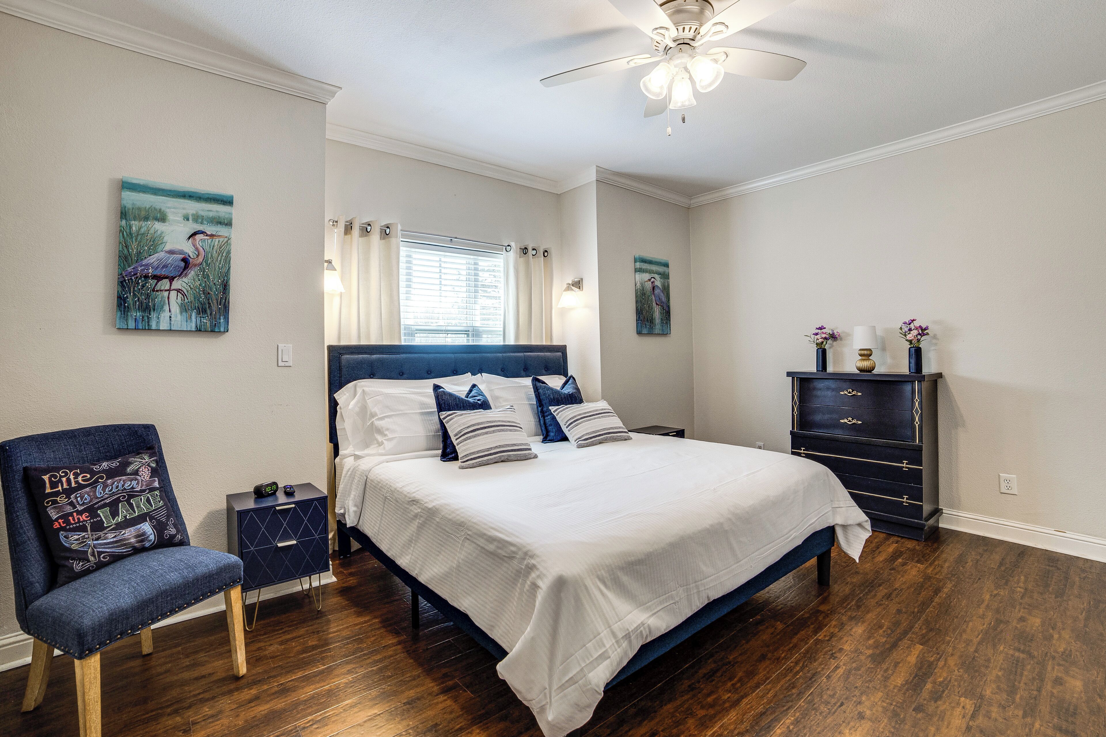 A bedroom with a bed, a chair, a nightstand, a dresser, and a ceiling fan.
