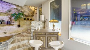A bathroom with a stone wall, a sink, two stools, a vanity with drawers, a lamp, and a window. - Walk to Beaver Lake! 'the Cavehouse' w/ 4 Decks (Garfield)