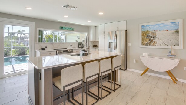 A modern kitchen with a large island, bar stools, and a view of a swimming pool.