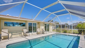 A covered swimming pool with lounge chairs and a house in the background.