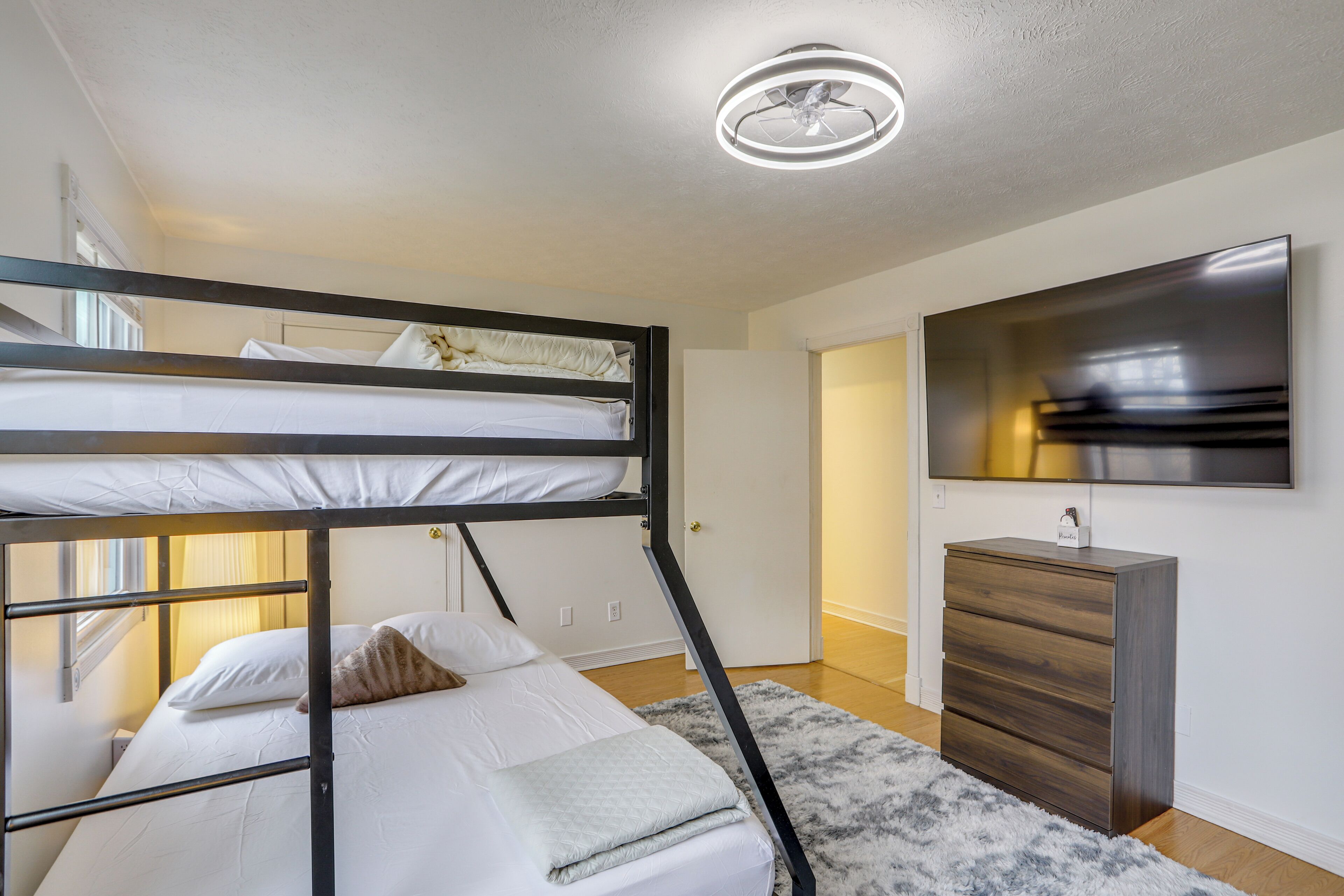 A bunk bed with a headboard, a dresser, a flat-screen TV, and a ceiling light fixture.