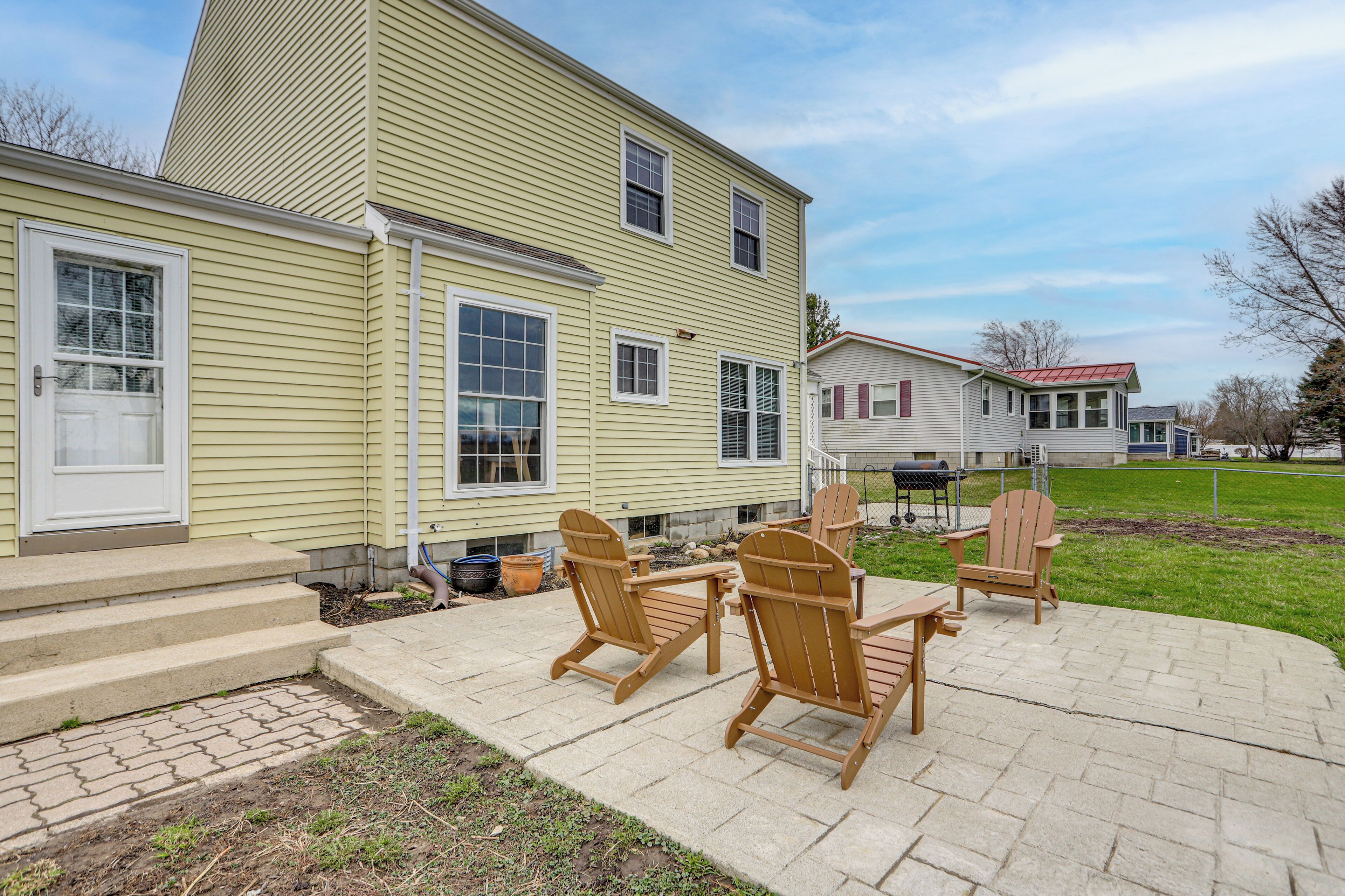 A two-story house with a patio area featuring Adirondack chairs and a table.