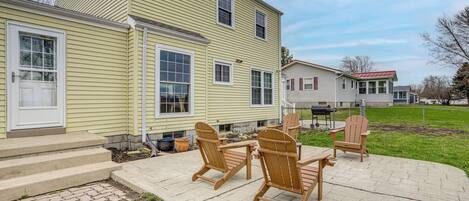 A two-story house with a patio area featuring Adirondack chairs and a table.