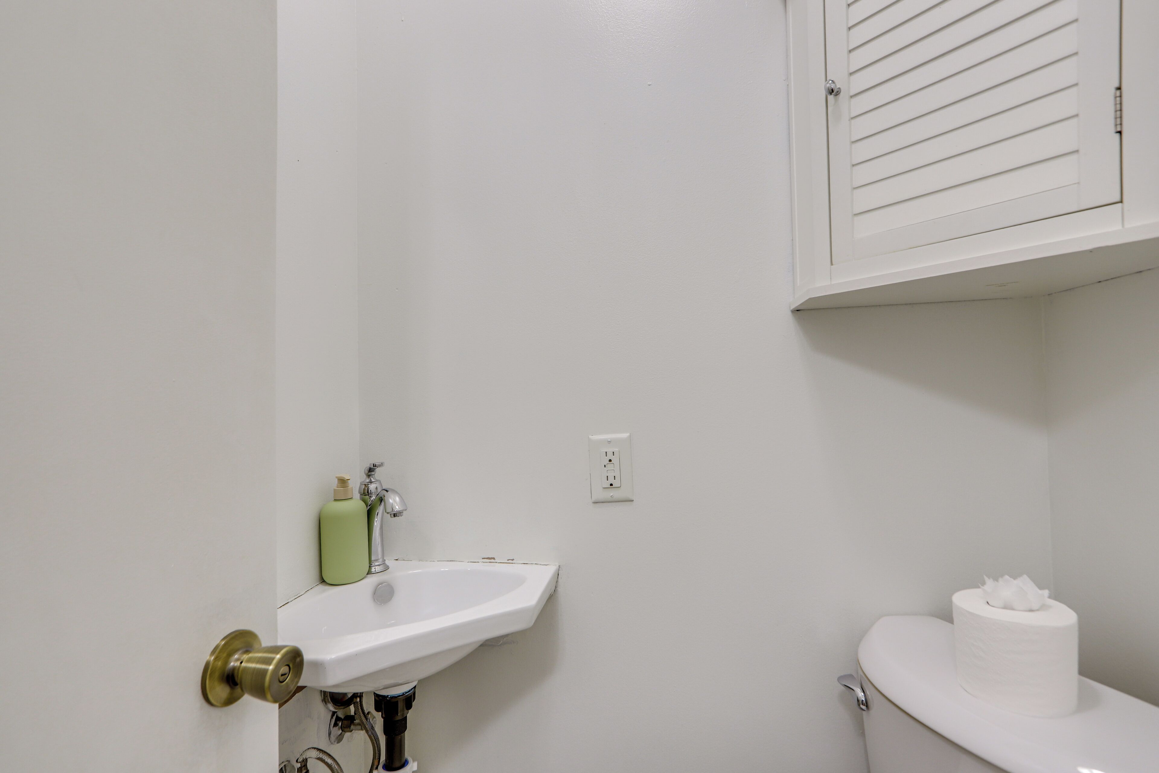 Une salle de bain avec un lavabo blanc, des toilettes et une bouteille verte posée sur le lavabo.