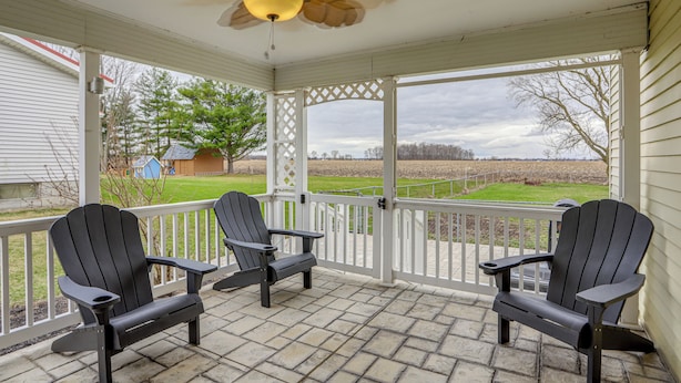Un portico coperto con due poltrone Adirondack, una ventola a soffitto e vista su un prato.