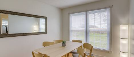 A dining area with a table, chairs, a potted plant, and a window with blinds.