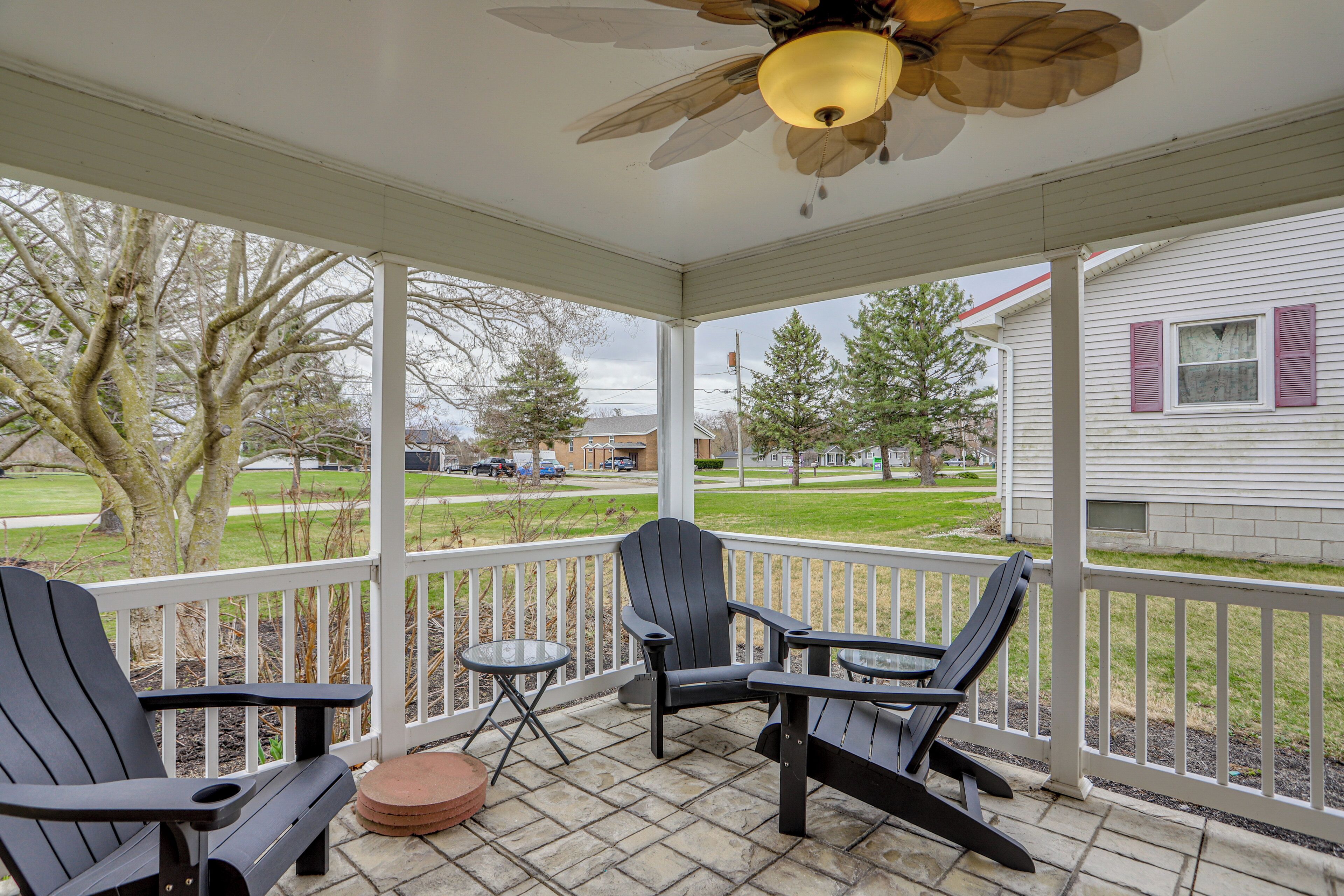A covered porch with Adirondack chairs, a small round table, and a ceiling fan.