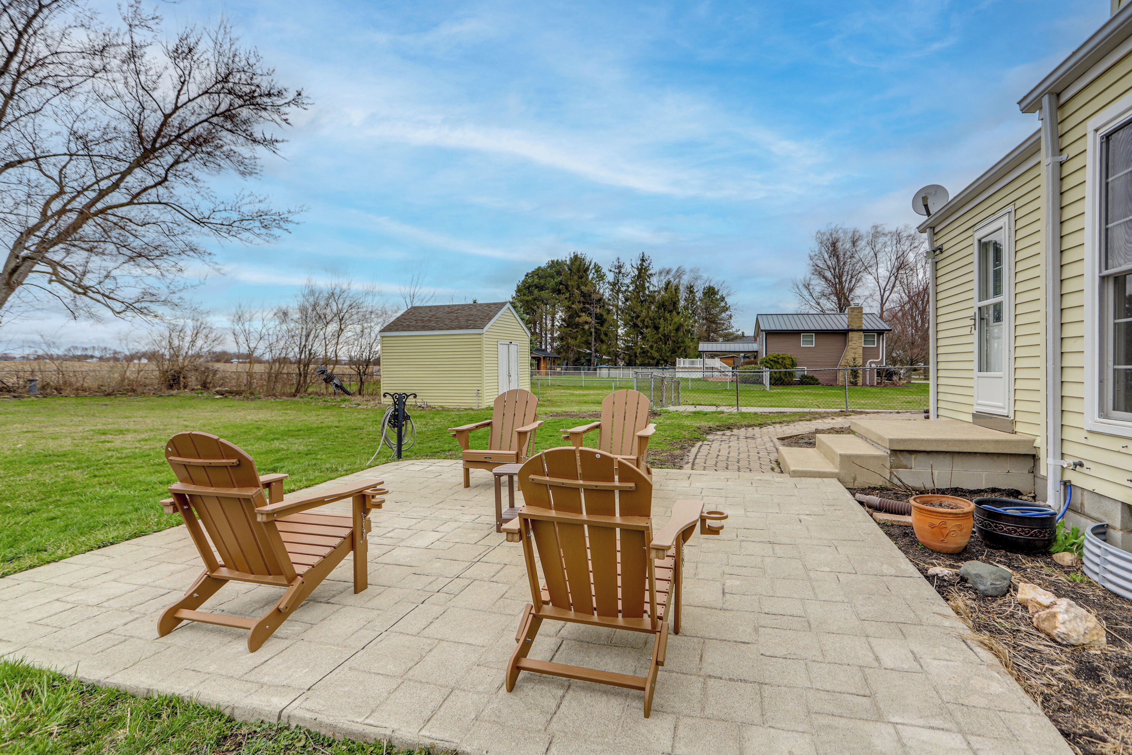 A patio with Adirondack chairs, a concrete pathway, and a house in the background.