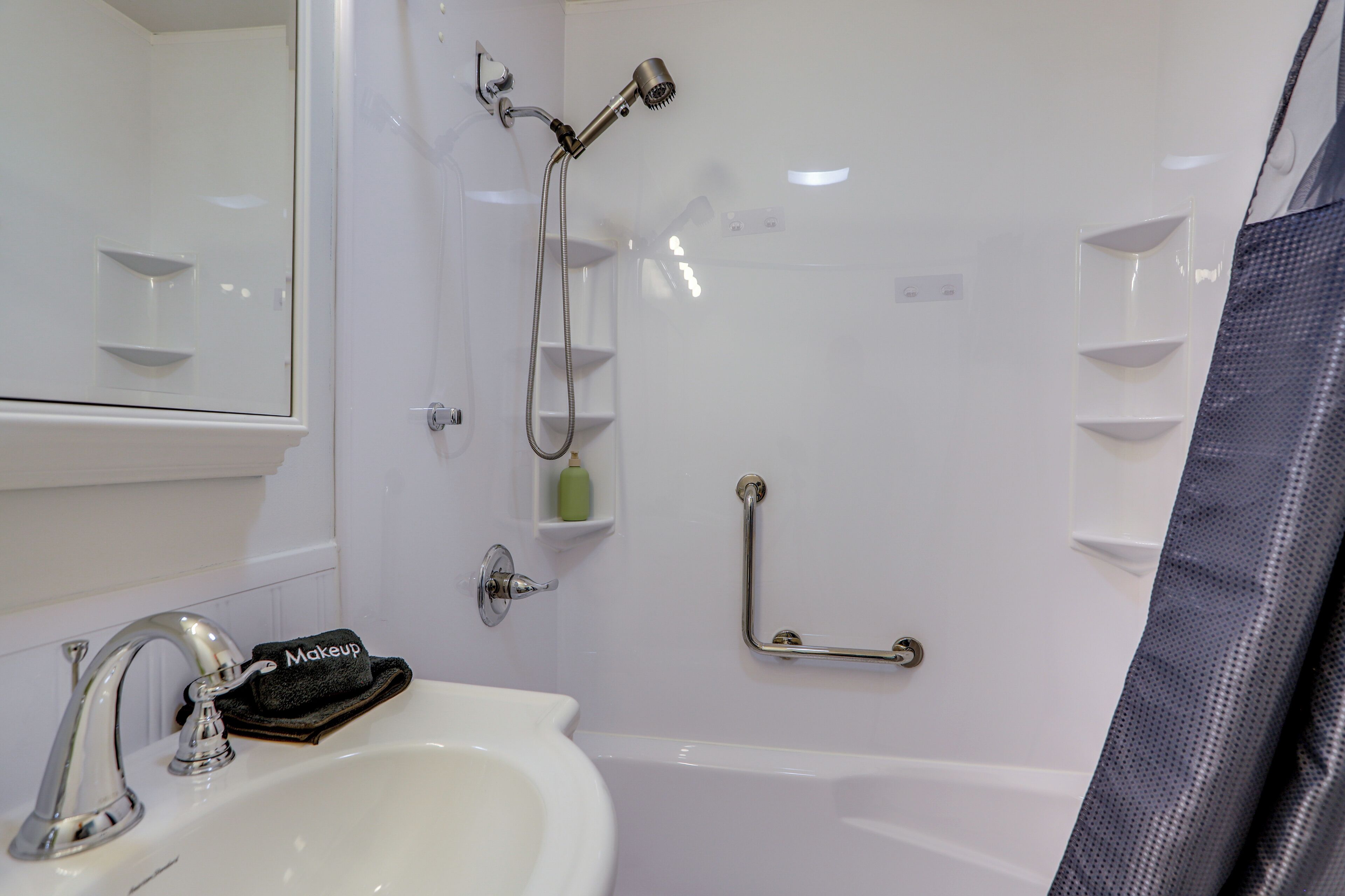 A bathroom with a sink, mirror, shower, and grab bars.