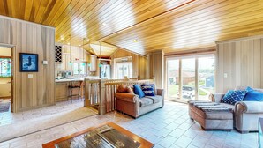 A spacious living area with a wooden ceiling, a kitchen with a bar, and a large window offering a view of the outside. - The Boat House w/ Dock: Enjoy Lake Life! (Syracuse)