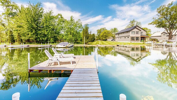 A wooden dock extending into a calm lake with a house in the background. - The Boat House w/ Dock: Enjoy Lake Life! (Syracuse)
