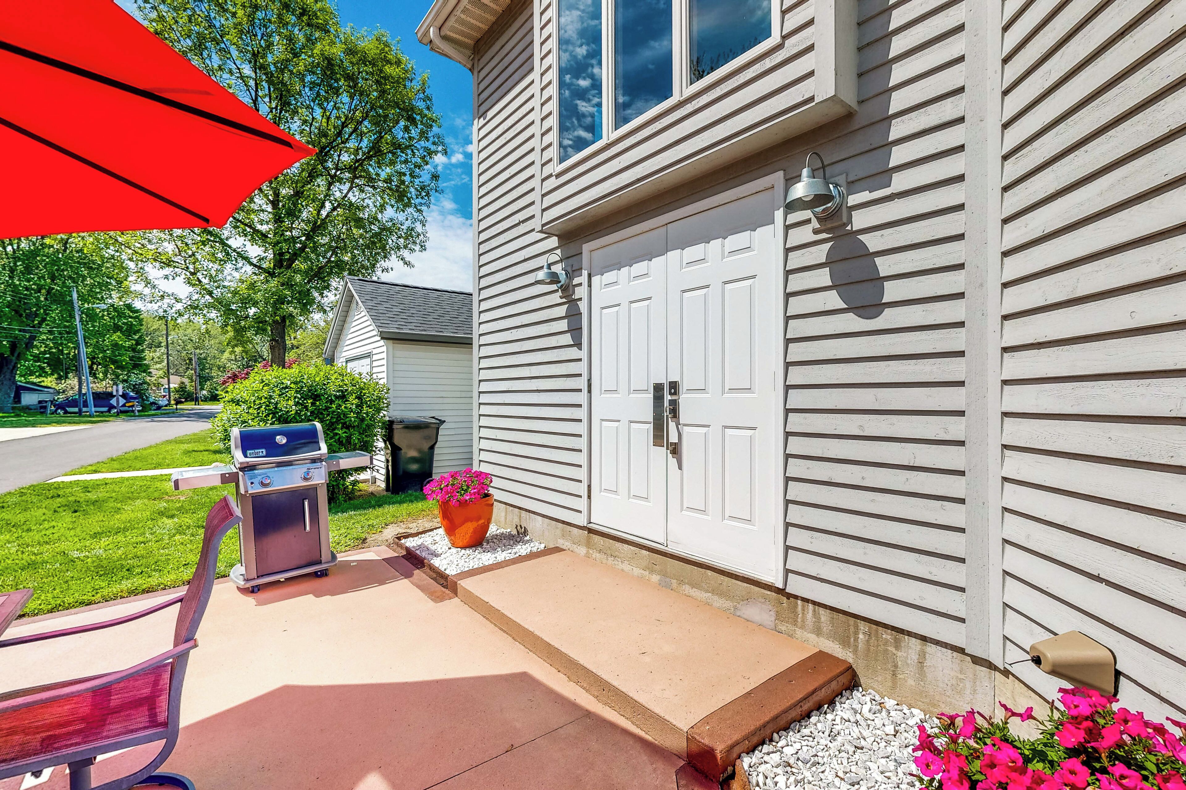 A house with a front porch, a barbecue grill, a potted plant, and a red umbrella.
