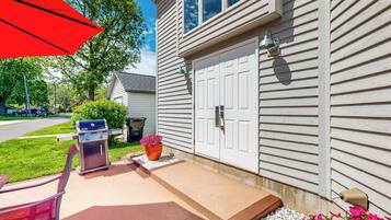 A house with a front porch, a barbecue grill, a potted plant, and a red umbrella.