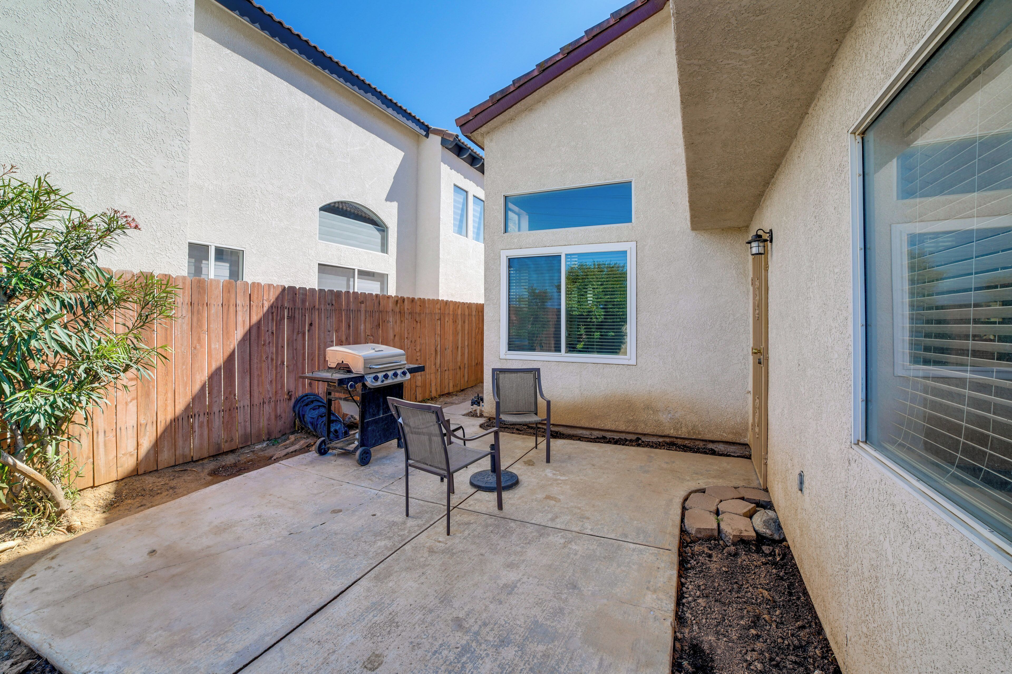 Une terrasse avec un barbecue, deux chaises et une clôture en bois.