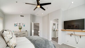 Un dormitorio moderno con cama, ventilador de techo, televisor montado en la pared y una escalera que conduce a otra habitación.