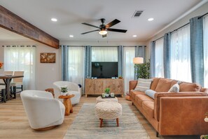 A modern living room with a sofa, armchair, ottoman, and a television on a wooden cabinet. - Downtown Modesto Gem! Updated Family Home (Modesto)