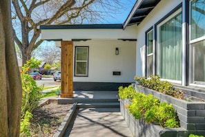 A modern building with a concrete pathway leading to a wooden door, large windows, and a small garden area with plants.