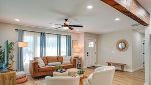 Una sala de estar con un sofá marrón, sillones blancos, una mesa de centro de madera y un ventilador de techo.