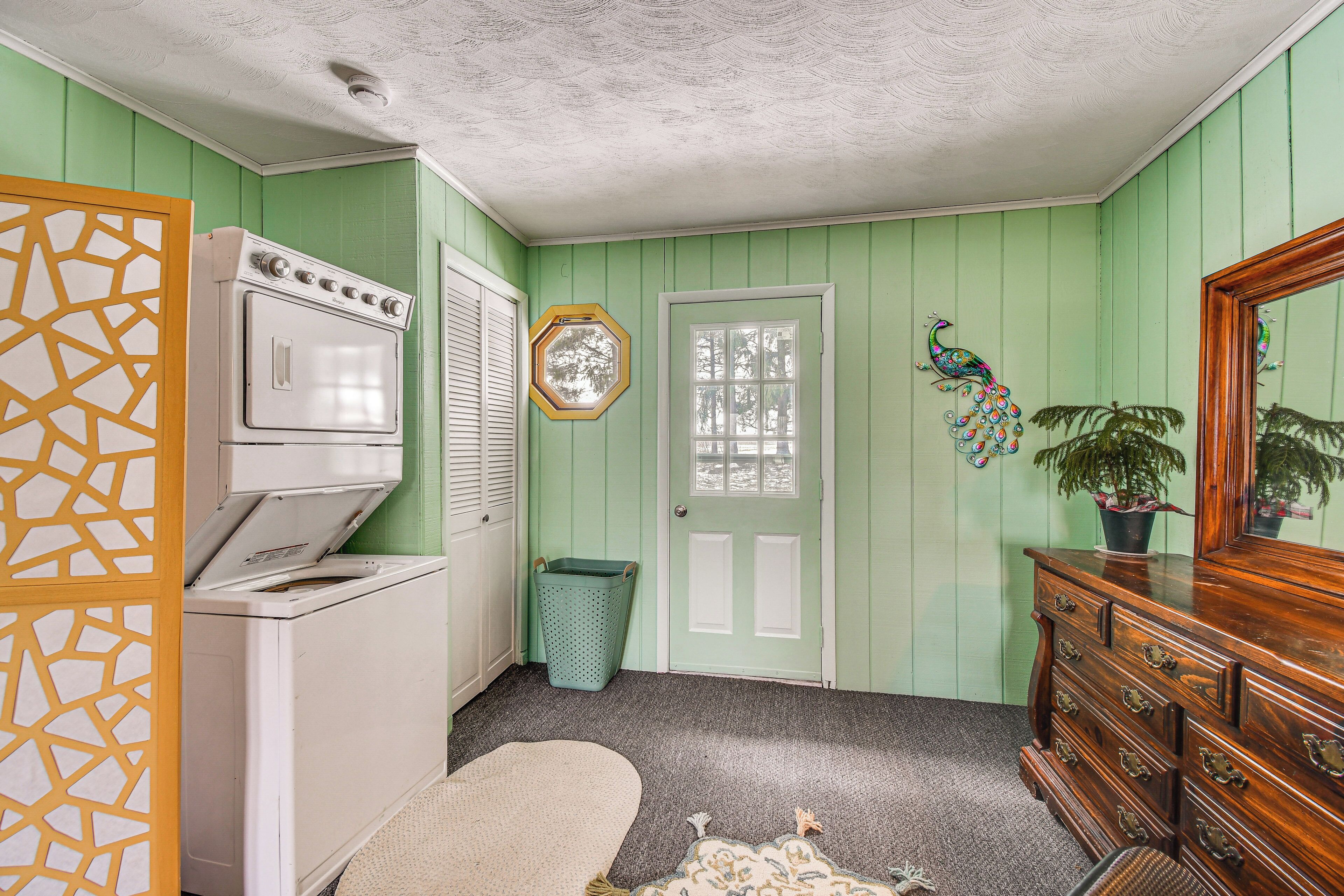 Une buanderie équipée d’un lave-linge et d’un sèche-linge, d’une poubelle, d’une porte avec une fenêtre et d’une commode avec un miroir.