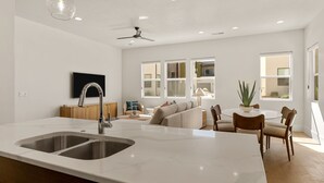A modern kitchen with a large island, a dining area with a round table and chairs, and a living room with a sofa and a TV. - Villa #44 at Bloomington Country Club: Pool, Golf, Restaurant (St. George)